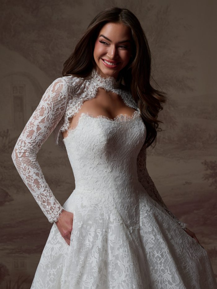 A bride wears the Serena gown by Maggie Sottero, a lace A-line dress with a high lace collar, cutout sweetheart bodice, and long lace sleeves.