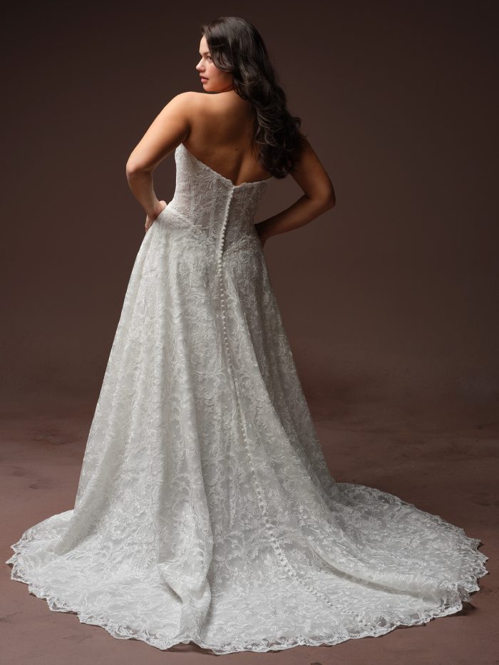 Maggie Sottero Zahia A-line wedding dress in ivory, curve fit — back view showing strapless lace bodice with covered button closure over zipper, full lace A-line skirt with scalloped hem and chapel train.