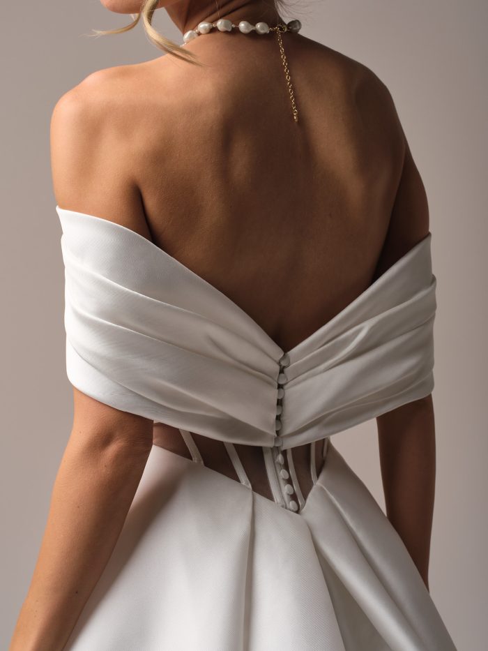 Close-up back view of the Brooke gown by Rebecca Ingram, showing the draped off-shoulder back detail and corset lacing at the waist.