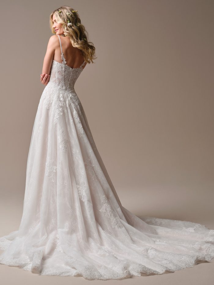 Rebecca Ingram Esmeralda A-Line wedding dress in ivory, back view showing open low back with sheer illusion lace bodice and delicate lace spaghetti straps, flowing tulle A-line skirt with scattered lace appliqués, and cathedral train with scalloped lace border.