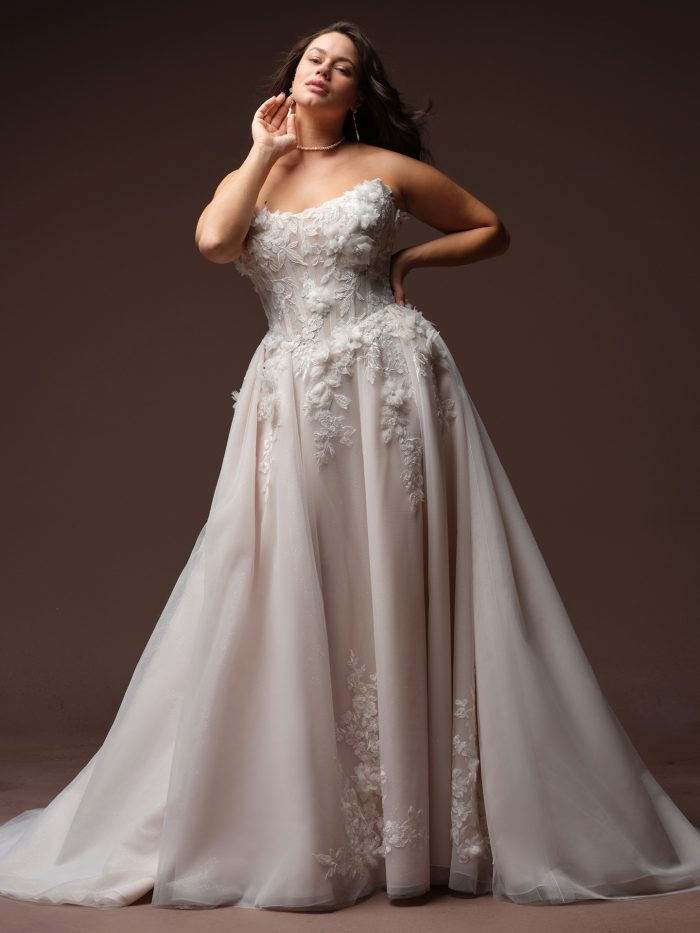 Rebecca Ingram Fleur ballgown wedding dress in ivory, curve fit — strapless sweetheart bodice with 3D floral lace appliqués over a full blush-tinted tulle ballgown skirt with sheer floral-embroidered overlay.