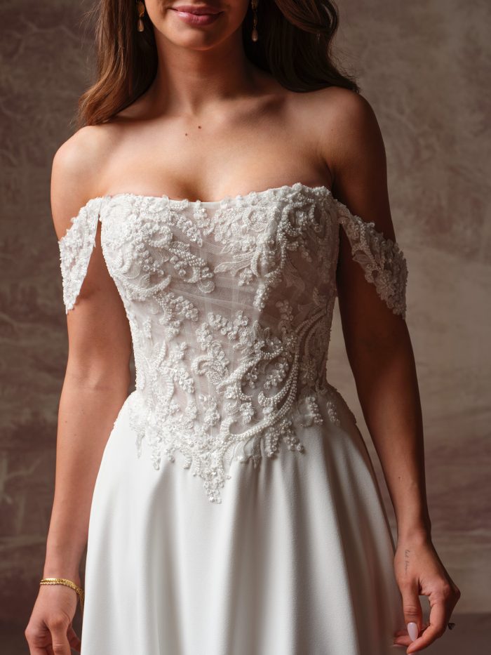Close-up of the Hazel A-line wedding dress, featuring an off-the-shoulder beaded lace bodice with a straight neckline, delicate draped shoulder straps, and a smooth satin A-line skirt.