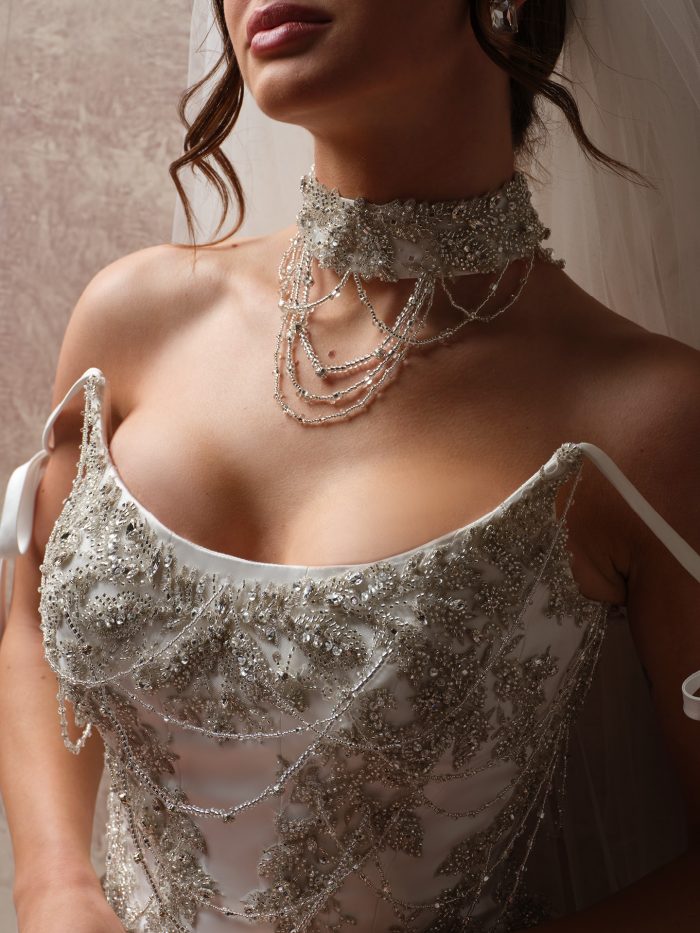 Close-up of the Aelarion beaded choker accessory, featuring a crystal and beaded band with cascading draped chain strands, worn over a beaded spaghetti-strap wedding dress bodice.