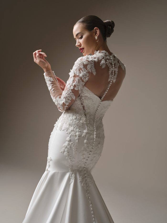 Back view of the Burke gown by Sottero and Midgley, showing the fitted mermaid silhouette with sheer lace back, covered buttons, and floral lace sleeve detail.
