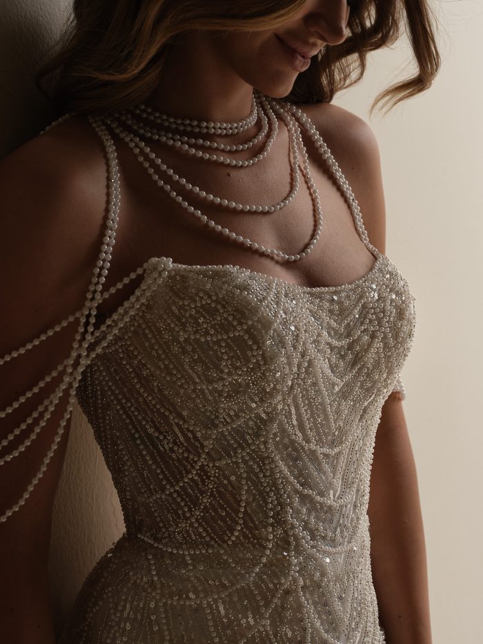 Close-up of the Constance sheath wedding dress, featuring a beaded and sequined bodice with a chevron pattern and delicate draped pearl strands cascading across the shoulders and back.