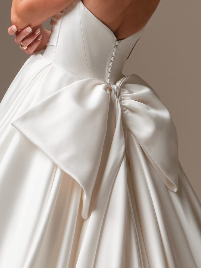 Close-up back view of the Elias gown by Sottero and Midgley, showing the covered button detail and dramatic asymmetrical satin bow.