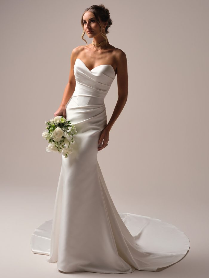 Front view of the Giselle Lane sheath wedding dress by Sottero and Midgley, featuring a draped strapless sweetheart neckline, fitted satin bodice, and slim sheath skirt with train, styled with a white bouquet.