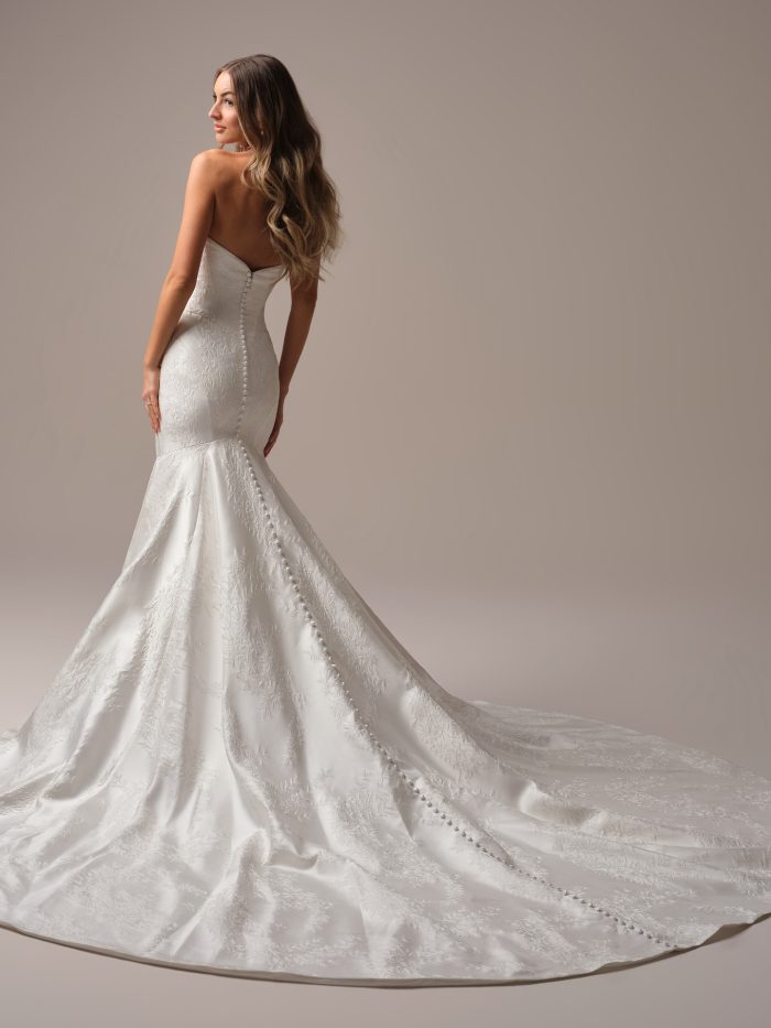 Back view of the Giselle Marie wedding dress by Sottero and Midgley, showing a strapless sweetheart back with covered button closure down the fitted floral jacquard mermaid skirt and train."