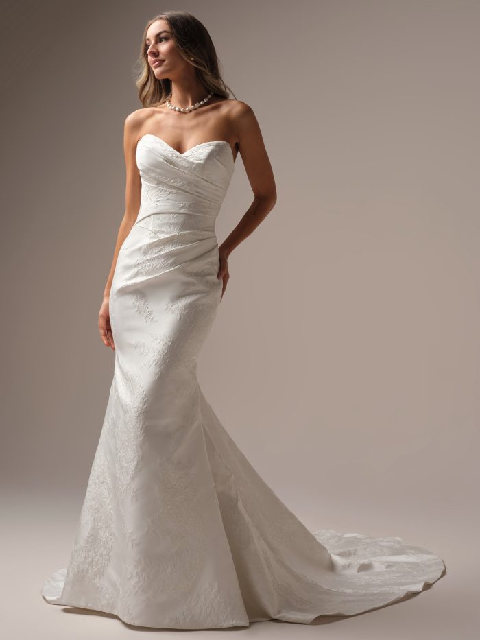 Front view of the Giselle Marie Lane sheath wedding dress by Sottero and Midgley, featuring a draped strapless sweetheart neckline and fitted floral jacquard mermaid skirt with train, styled with a pearl necklace.