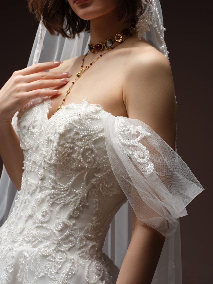 Another close-up of the Gwyneth gown by Sottero and Midgley, highlighting the beaded bodice, sheer off-shoulder puff sleeve, and jeweled necklace.