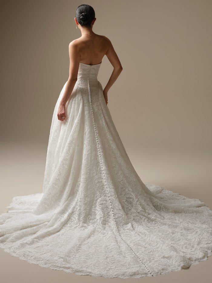 Sottero and Midgley Tamar A-Line wedding dress in white, back view showing open back with covered button closure running the length of the cathedral train, and full all-over ornate lace A-line skirt with sweeping scalloped lace cathedral train.
