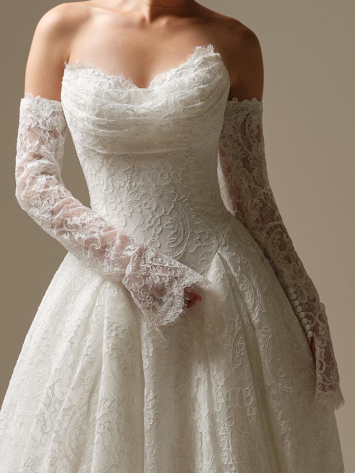 Close-up of the Tamar detachable lace sleeves accessory, featuring sheer long sleeves with floral and paisley lace embroidery and button cuff detailing, layered over a strapless lace bodice and full skirt.