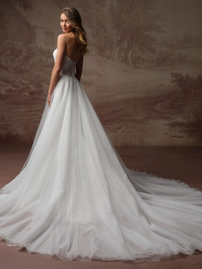 Back view of a bride in a strapless lace wedding dress with a detachable tulle overskirt train sweeping behind her.