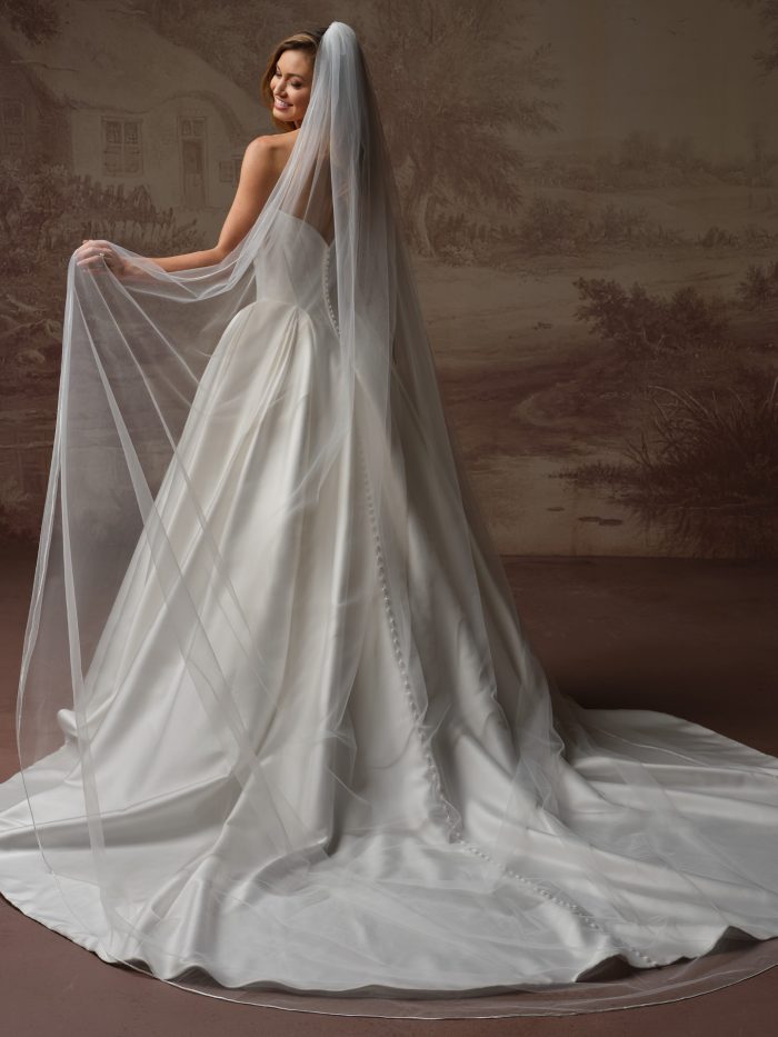 Bride pulling out the edge of the Amor cathedral wedding veil by Maggie Sottero from the Essentials Edit collection, worn over a strapless satin ball gown with a sweeping train.