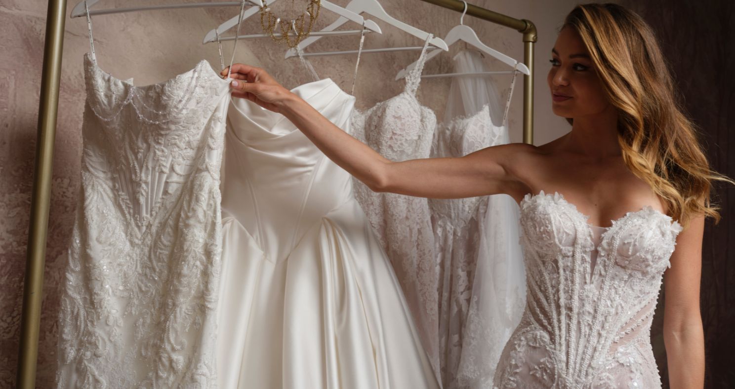 A bride wearing the Stasia dress by Maggie Sottero, a strapless wedding dress with a beaded lace bodice, browses a rack of wedding gowns.