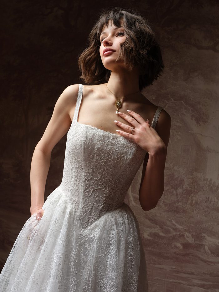 Close-up of the Autumn ballgown wedding dress by Maggie Sottero, showing the straight-across lace bodice, thin straps, and floral lace texture on the fitted waist.