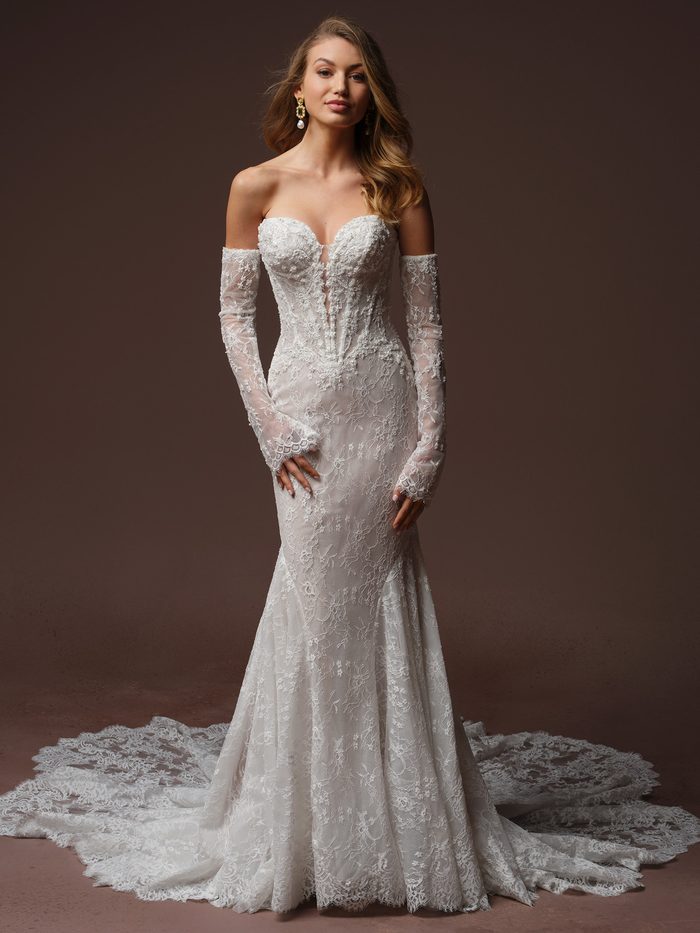 Bride wearing the Bellevue Royale fit-and-flare wedding dress by Maggie Sottero, featuring an off-the-shoulder beaded lace bodice with detachable lace gloves and a fitted lace skirt with a dramatic train.