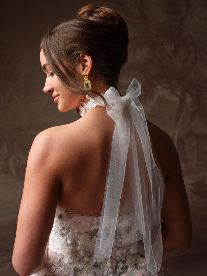 Back-view bridal fashion portrait showcasing the Benton choker by Maggie Sottero, designed with a romantic tulle bow and flowing streamers, paired with rectangular crystal drop earrings and a floral appliqué ballgown wedding dress.