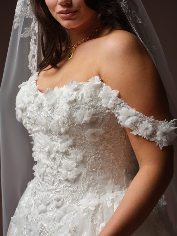 Close-up of the Benton wedding dress by Maggie Sottero, showing the off-the-shoulder 3D floral lace bodice and cap sleeve detail.