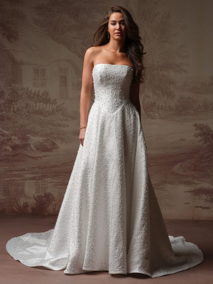Front view of a bride wearing the Elowyn A-line wedding dress by Maggie Sottero, featuring an all-over pearl-beaded strapless bodice and a flowing pearl-beaded skirt with a train.