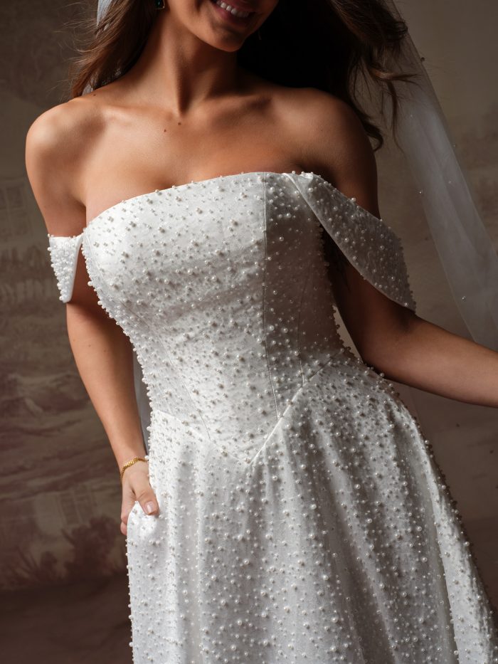 Close-up of the Elowyn A-line wedding dress by Maggie Sottero, showing the fully pearl-beaded bodice and skirt with off-the-shoulder cap sleeve.