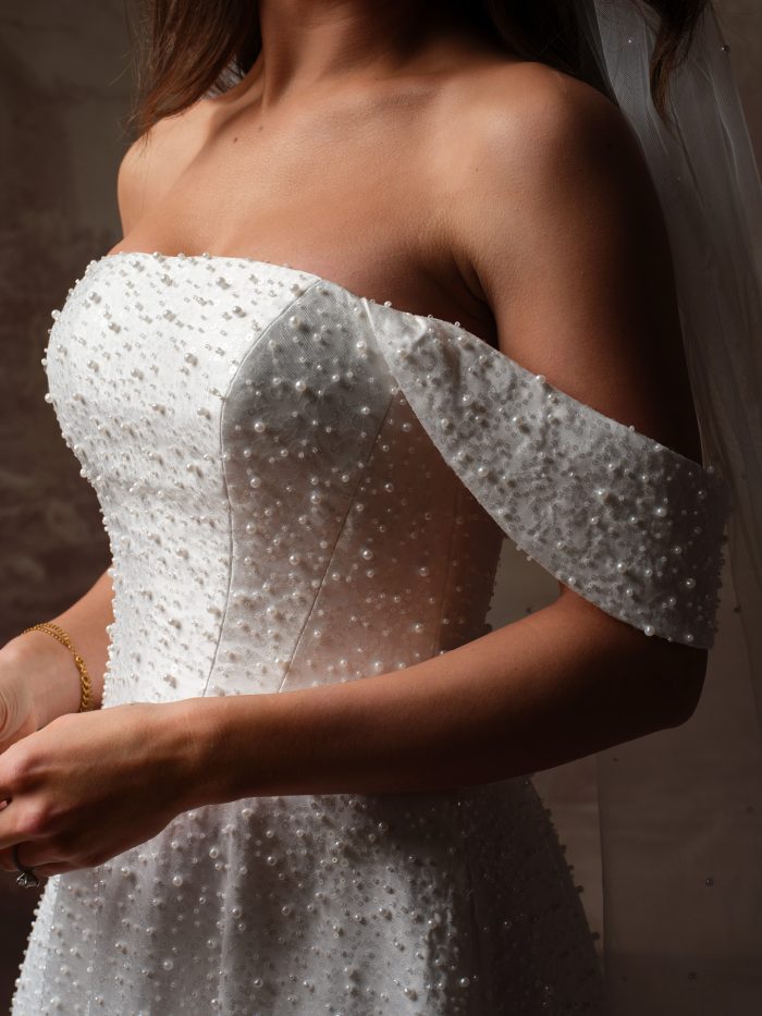 Close-up of the Elowyn wedding dress by Maggie Sottero, showing the pearl-beaded bodice and off-the-shoulder cap sleeve.