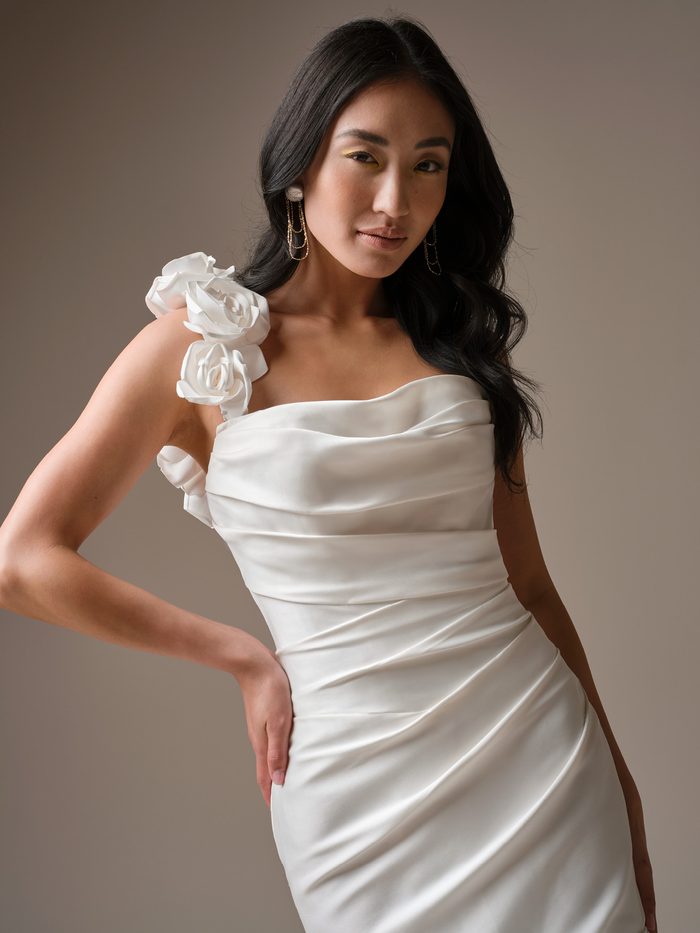 Close-up of the Emelina fit-and-flare wedding dress by Maggie Sottero, showing the ruched satin bodice with a floral rosette shoulder strap.