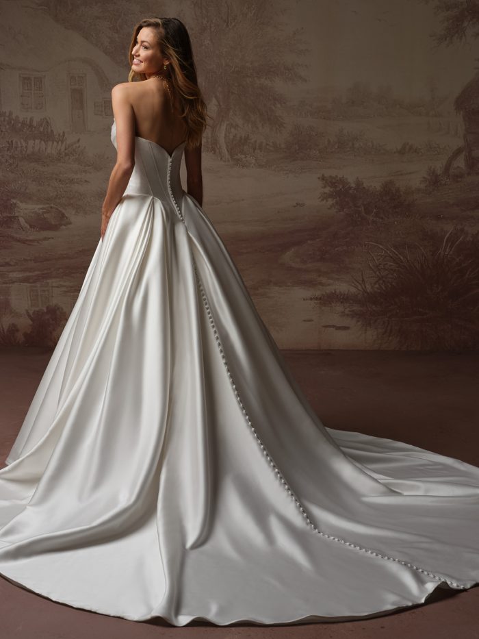 Back view of bride wearing the Fiorita strapless satin ballgown wedding dress by Maggie Sottero, featuring a sweetheart back neckline, covered button closure, and a dramatic full skirt with cathedral train.