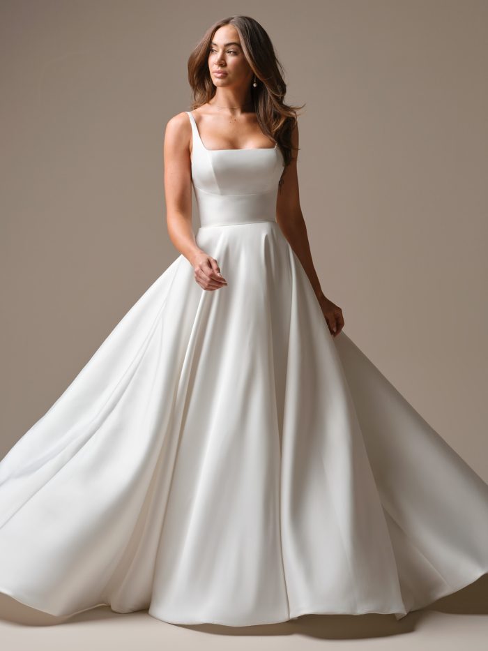 Front view of a bride wearing the Galina A-line wedding dress by Maggie Sottero, featuring a square neckline with slim straps, a fitted satin bodice, and a smooth flowing skirt with a train.