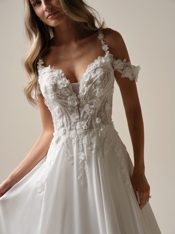 Close-up of the 3D floral lace bodice and cold-shoulder straps on the chiffon Hunter wedding dress by Maggie Sottero.