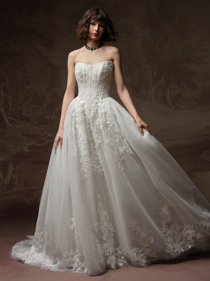 Bride wearing the Lyra ballgown wedding dress by Maggie Sottero, featuring a strapless lace bodice and a full tulle ballgown skirt with floral lace appliqués and a train.