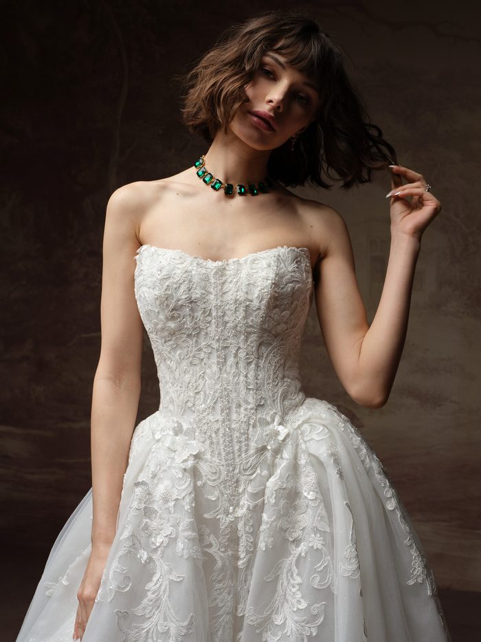 Close-up of the Lyra ballgown wedding dress by Maggie Sottero, showing the strapless lace bodice with beaded detail and floral embroidery.