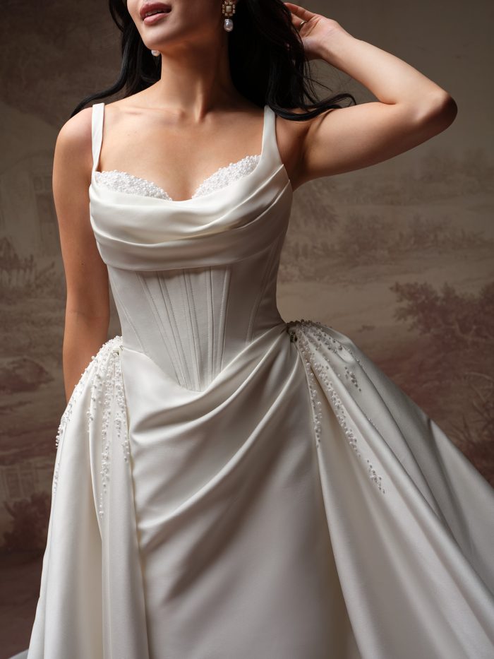 Close-up of the Melissa Royale wedding dress by Maggie Sottero, showing the beaded cowl neckline, corset boning, and pearl-beaded pickups gathering the satin ball gown skirt.