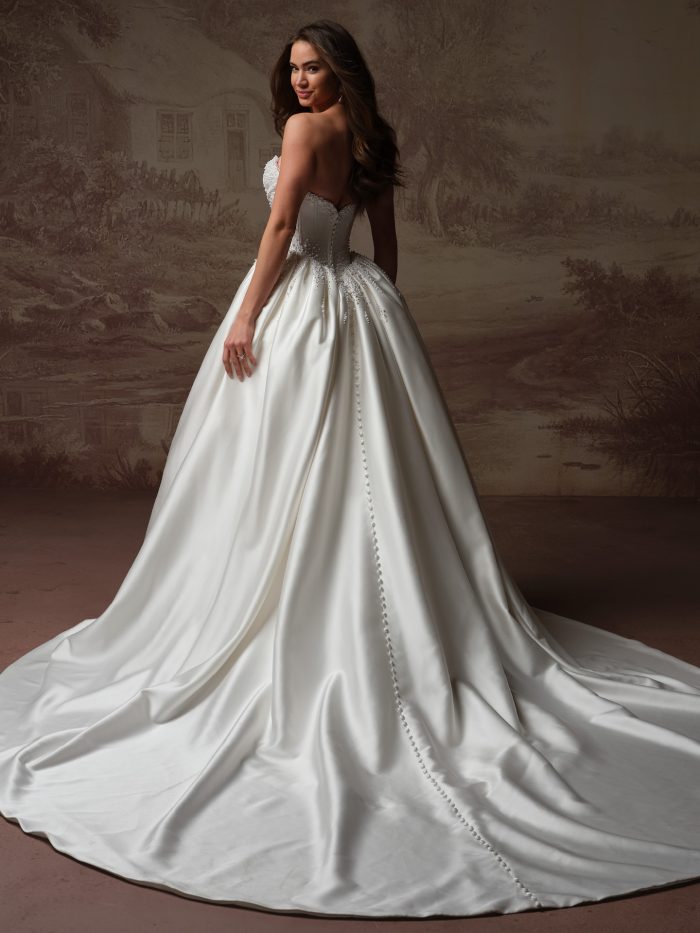 Back view of bride wearing the Melissa Royale strapless satin ballgown by Maggie Sottero with a detachable train, featuring a beaded bodice, sweetheart back neckline, and covered button closure.