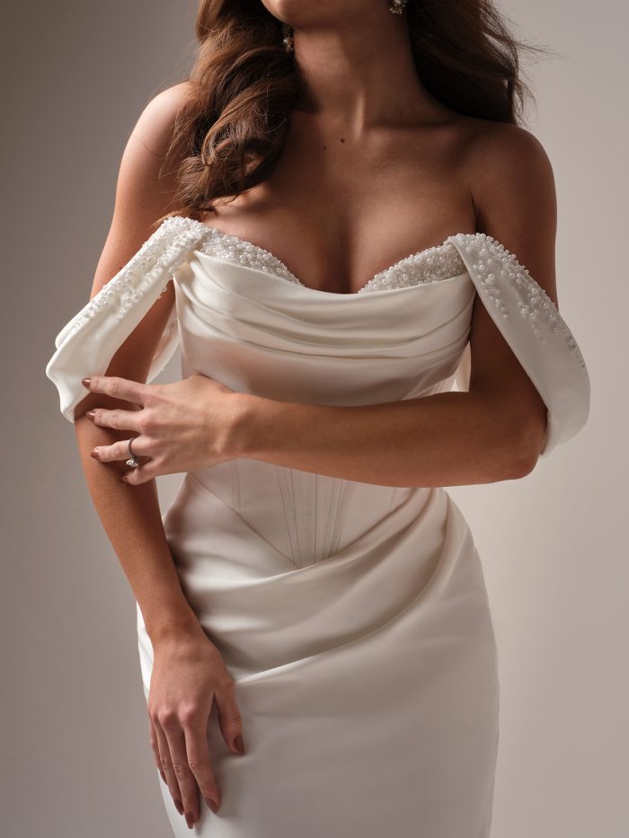 Close-up of the Melissa cap sleeve topper by Maggie Sottero, showing the pearl-beaded off-the-shoulder neckline and draped satin bodice over a corseted fitted skirt.