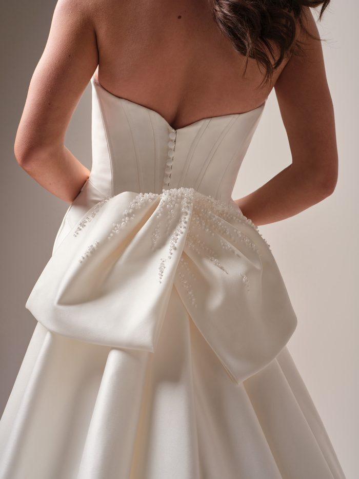 Close-up of the Melissa wedding dress by Maggie Sottero, showing the sweetheart corset back with covered buttons and a beaded satin bow accenting the detachable train.