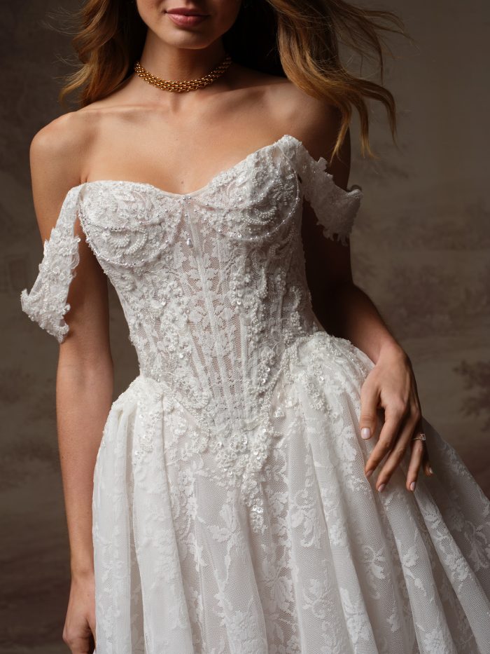 Close-up of a bride wearing the Ryland wedding dress by Maggie Sottero, showing the beaded lace bodice, sweetheart neckline, and off-the-shoulder sleeves in detail.