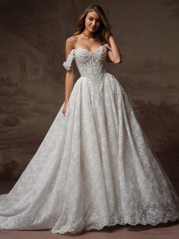 Front view of a model wearing the Ryland Ballgown Wedding Dress by Maggie Sottero in ivory, featuring an off-the-shoulder beaded lace bodice with sweetheart neckline and detached cap sleeves, paired with a full lace ballgown skirt with a scalloped hem.