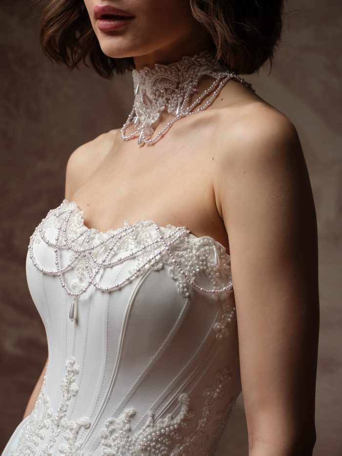 Front detail of the Seattle wedding dress by Maggie Sottero, showing a beaded lace choker with cascading pearl draping that is like the strapless ballgown's beaded and pearl-trimmed sweetheart neckline.
