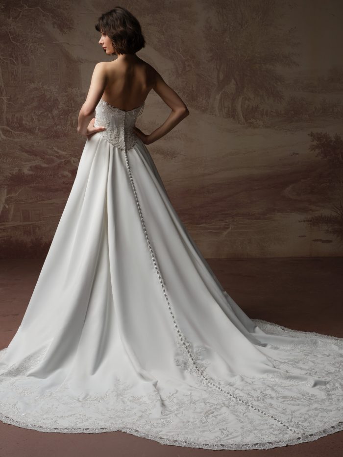 Back view of bride wearing the Seattle strapless satin ballgown wedding dress by Maggie Sottero, featuring a beaded bodice, sweetheart back neckline, covered button closure, and an embellished train.