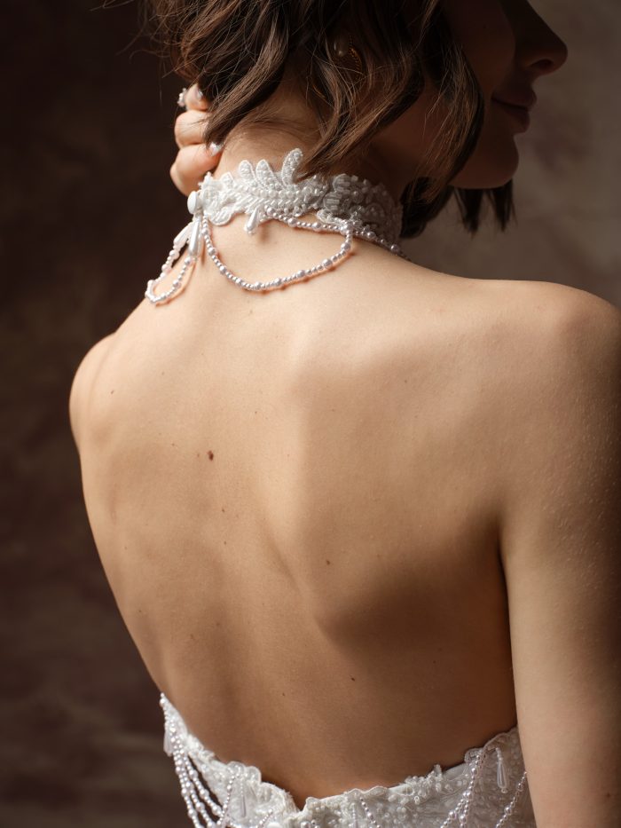 Back view of the Seattle by Maggie Sottero, highlighting the beaded lace choker with layered pearl strands draping down the open back of the strapless wedding dress.