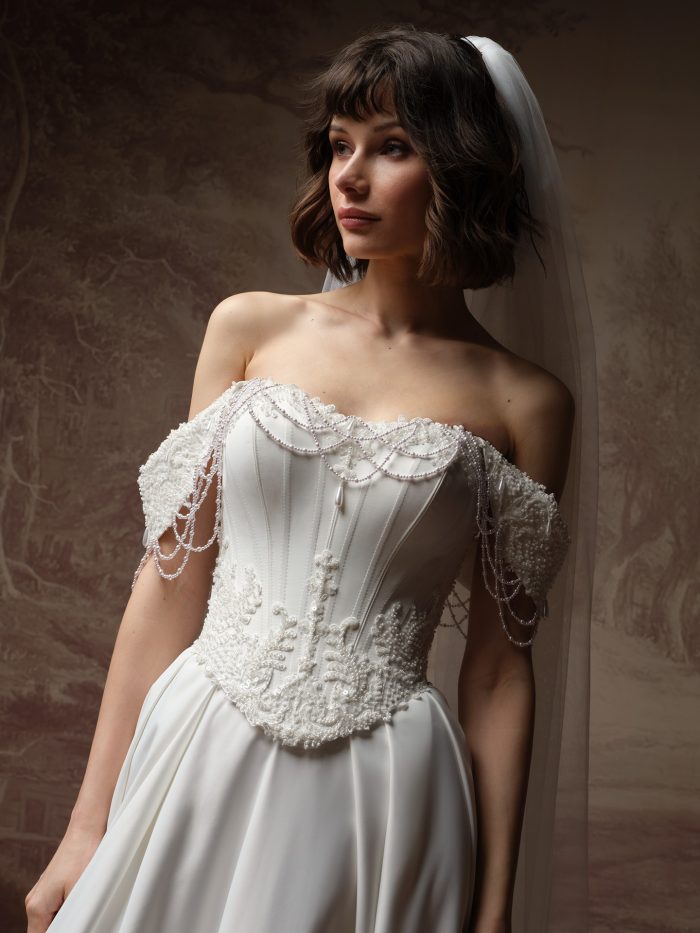 Close-up of the Seattle wedding dress by Maggie Sottero, showing the corset bodice with lace and pearl-draped off-the-shoulder cap sleeves.