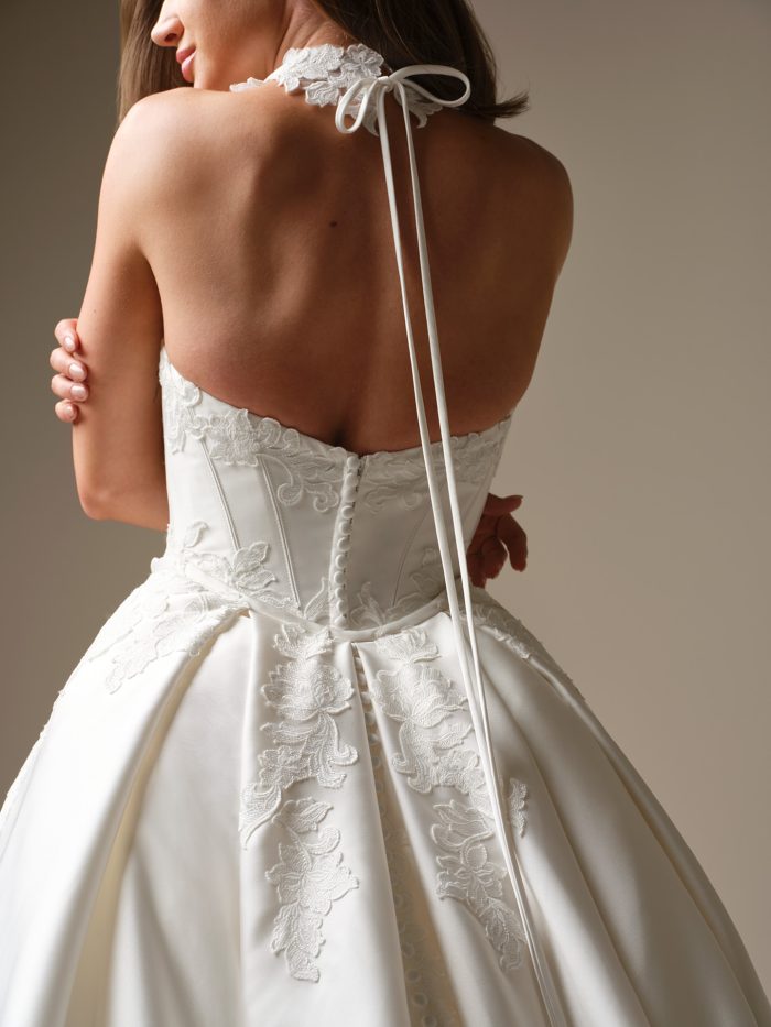 Back view of the Serafina Lane fit-and-flare wedding dress by Maggie Sottero, featuring a lace-appliquéd satin corset bodice, covered button detailing, and a floral lace bridal choker tied with long ribbon tails.