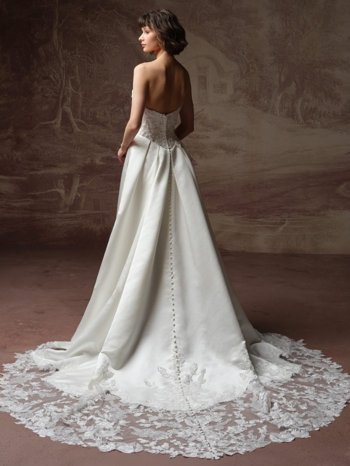 Back view of bride wearing the Wisteria strapless satin A-line wedding dress by Maggie Sottero, featuring a lace bodice, covered button closure, and an illusion lace train.
