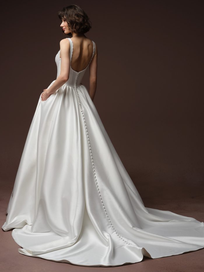 Back view of the Zurielle A-line wedding dress by Maggie Sottero, showing a low scoop back with beaded strap trim and a row of covered buttons running down the train.