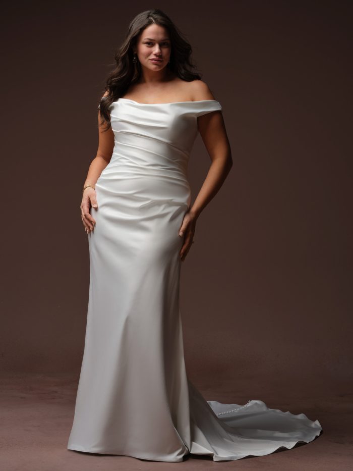 Clementine by Rebecca Ingram sheath wedding dress with an off-the-shoulder neckline, flattering ruched satin bodice, and sleek minimalist bridal silhouette.