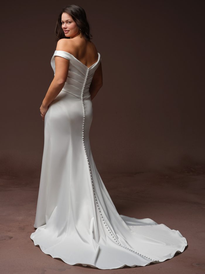 Clementine by Rebecca Ingram satin wedding gown with an off-the-shoulder back, covered button detailing, fitted silhouette, and elegant chapel-length train.