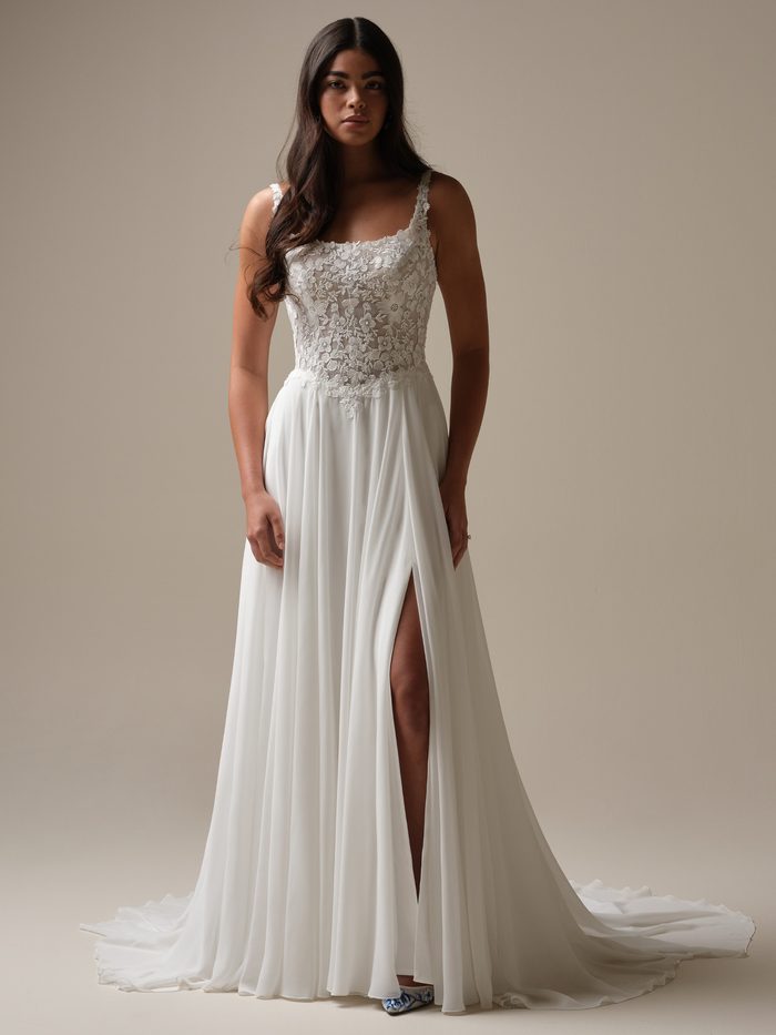 Bride wearing the chiffon Cory A-line wedding dress by Rebecca Ingram, featuring a floral lace bodice with square straps and a flowing skirt with a leg slit and train.