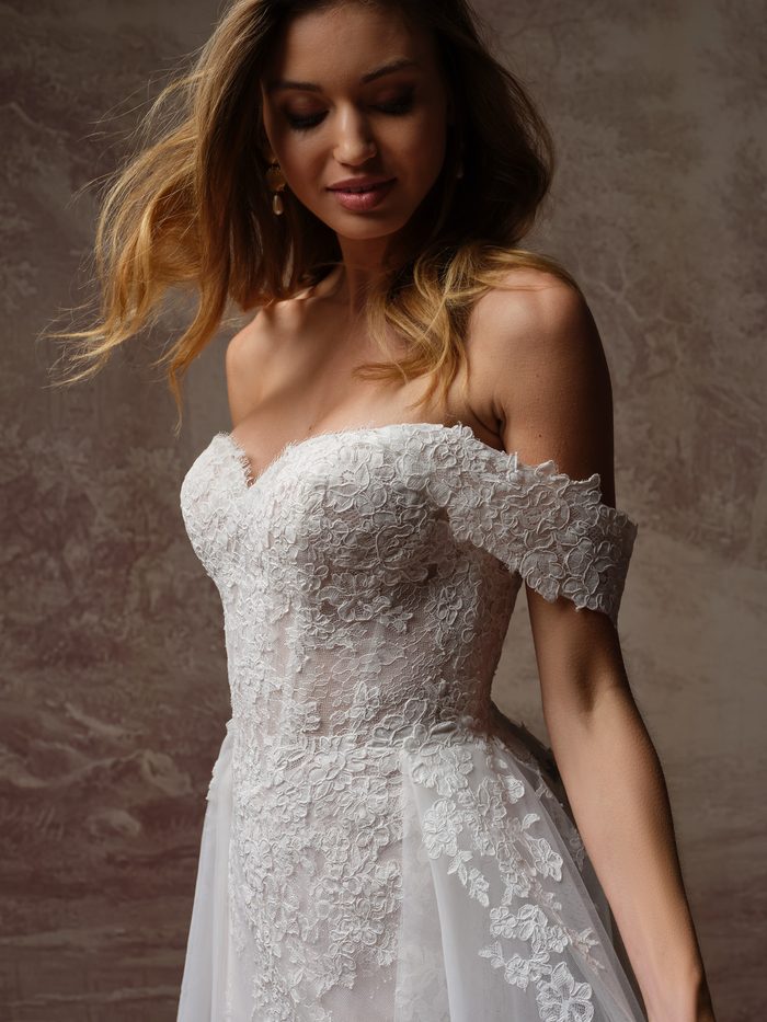 Close-up of the Esmeralda Lane fit-and-flare wedding dress by Rebecca Ingram, shown with off-the-shoulder lace sleeves and a floral lace bodice.