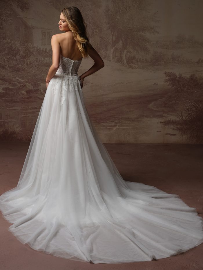 Back view of bride wearing the Esmeralda Lane strapless lace A-line wedding dress by Rebecca Ingram with a detachable tulle train, featuring a lace bodice and sweetheart back neckline.